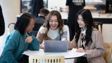 three students sat at a table looking at a laptop
