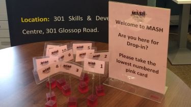 Pink appointment cards on a wooden table with MASH signs in the background