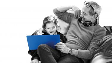 Father and young daughter sitting on sofa with a laptop