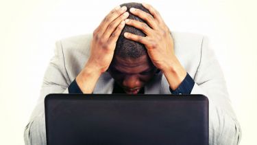 A photo of a man looking at a laptop with his head in his hands