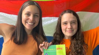 Two young women in front of a Dutch flag with their course book