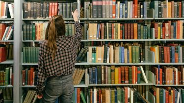 A student choosing a book from the shelves in the University Library.