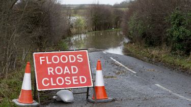 A flooding road in the UK countryside with a road closed sign