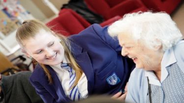A photo of an elderly woman laughing whilst talking to a young girl who is smiling.