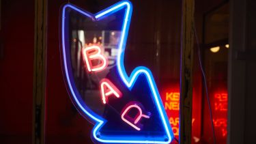 A blue neon outline of an arrow with the word BAR in pink neon lights
