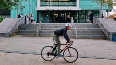 A man on a bike cycling on the leavygreave road cycle path past Information Commons building