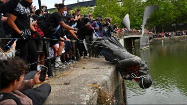 A group of protestors stand on Bristol harbourside, lowering the Colston statue into the river