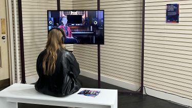 An individual sat on a white bench watching Objectified on a TV screen.