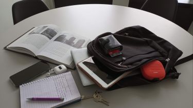 an open bag showing a laptop, ipad, purse with credit cards, headphones and keys