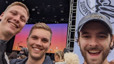 Three students posing in front of a big stage at a Swedish music festival