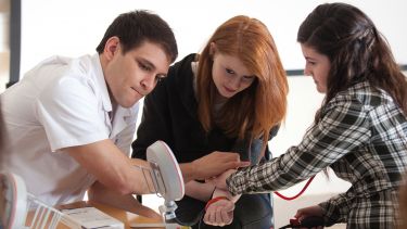 Three students sit looking at a monitor whilst taking their blood pressure