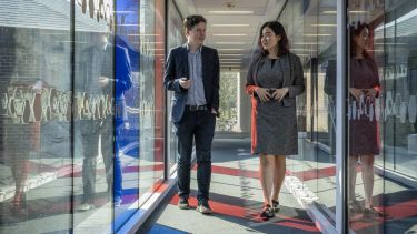 A white male and a Chinese female in business attire walking through a glass tunnel.