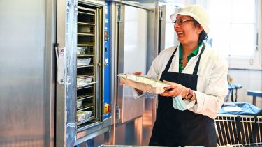 Woman in white coat and apron puts tray in oven