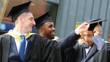 Three graduates looking happy and helping with hats