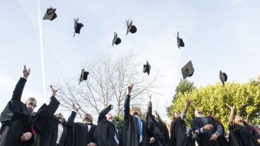 Image of graduates throwing hats in blue skies