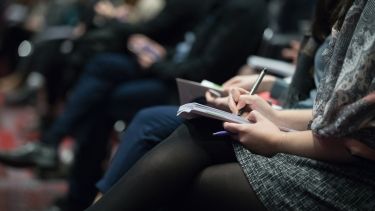 A line of people sat down, writing in notepads