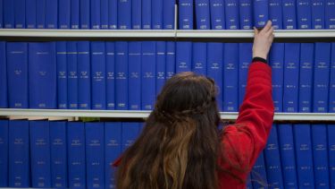 a girl in a red jacket reaching for a book from a shelf. 