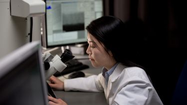 Kroto Centre PhD student at a computer and using equipment in a lab coat