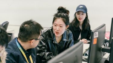 three students, sat at a computer, talking 