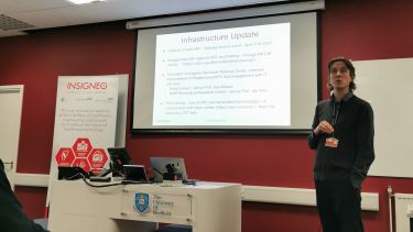 Andrew Narracot stood in front of a projector screen in a university workroom, speaking to Insigneo Members