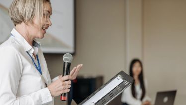 An image of a speaker, holding a microphone, giving a talk