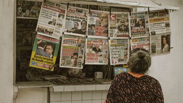 A woman at a news stand looking at a row of newspapers.
