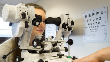 Patient on an eye-testing apparatus with an eye chart in the background