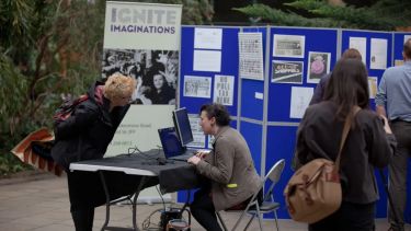 An outdoor festival exhibit in which two individuals are discussing the exhibit as others walk past. "Ignite Imaginations" appears in the background.