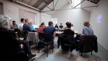 A group reviewing some content as part of a festival indoors, using a projected screen on a wall