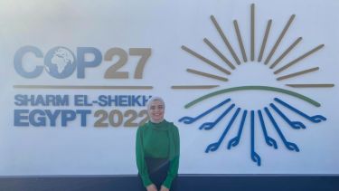 Photograph of Nada Adham standing next to the official logo for COP27 in Egypt