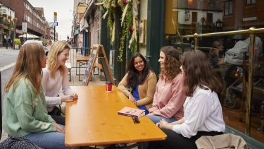 Five students sat around a table outside a cafe