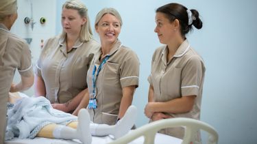 A group of nursing apprentices stood next to a hospital bed