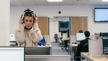 A girl sits in a computer room with a pair of headphone on. 