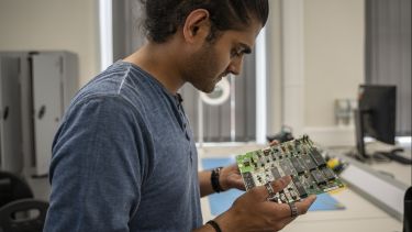 MSc student Ronak looking at a circuit board in a lab on campus