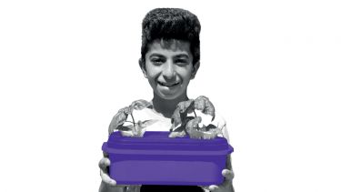 A refugee child is smiling as he holds a container growing crops.