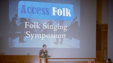 Folk Symposium speaker on stage with backdrop Access Folk - Folk Signing + Symposium