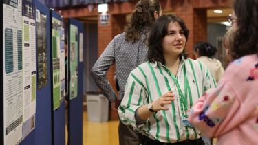A photo of Aimilia Kakampoura standing in front of a poster of her research.