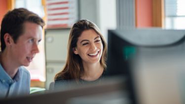 Two students working together behind a computer screen.