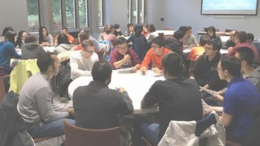 Several groups of students sitting at round meeting tables engaged in discussion