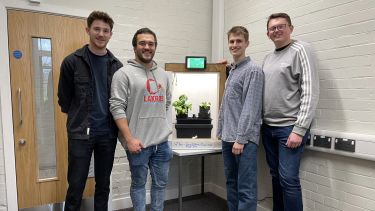 Photograph of Alex and other group members standing next to their final year project, a climate control system to grow plants inside a box