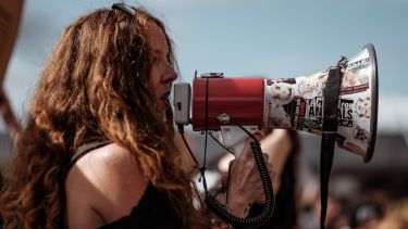 A woman with long curly hair talking into a megaphone.
