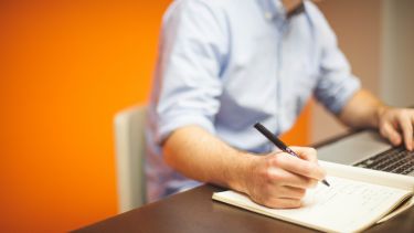 A man working on a laptop and a notebook.