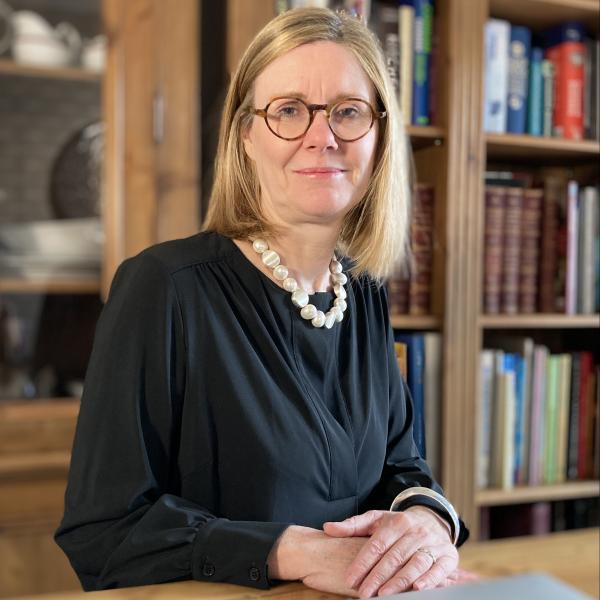 Profile picture of A head and shoulders photograph of Dr Samantha Drobinski. She is sat at a table wearing a black top and white beaded necklace. In the background is a bookcase.