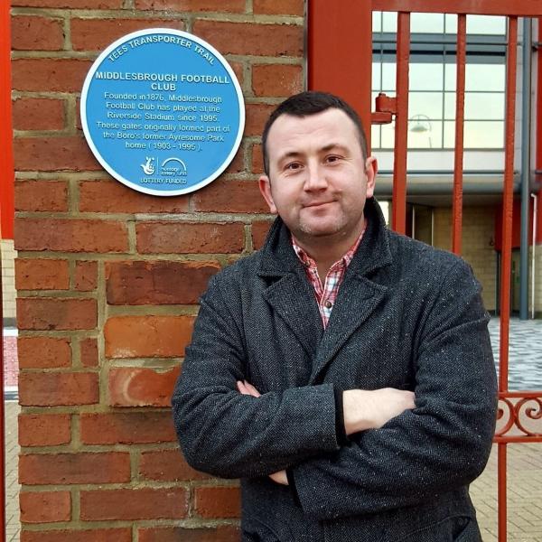 Profile picture of Dr Tosh Warwick next to a heritage sign for Middlesbrough Football Club