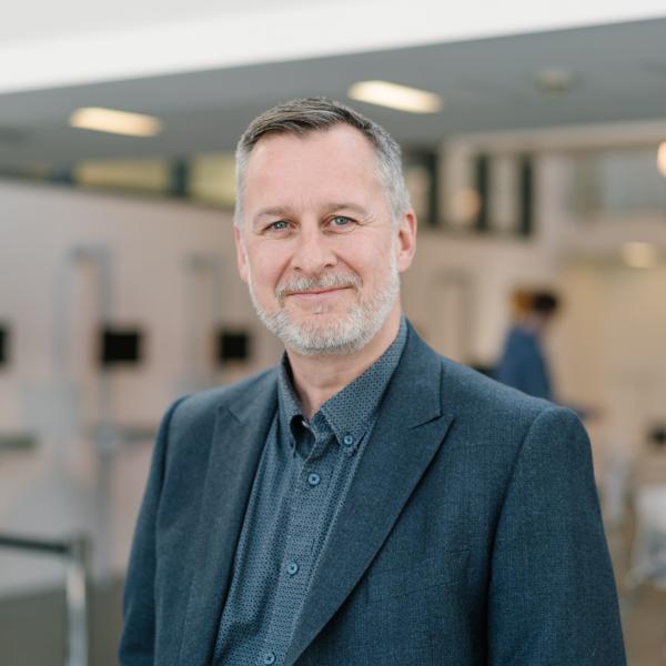 Profile picture of Damian Hodgson wearing a grey shirt and dark grey jacket.