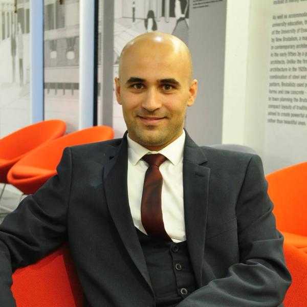 Profile picture of Ahmad Abras sat down on a red chair wearing a suit.