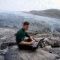 Alumnus Olly Bartlett sitting with a laptop in front of an ice sheet