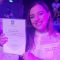 Andra-Maria smiling, at her graduation after-party, holding her certificate