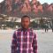 A profile photo of alumni, Saleh. He is wearing a plaid shirt and standing in front of some red rocks. 