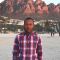 A profile photo of alumni, Saleh. He is wearing a plaid shirt and standing in front of some red rocks.